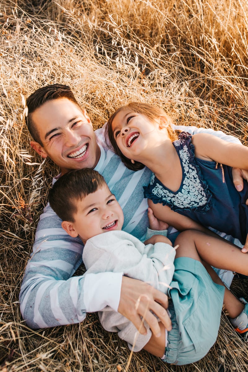 Family Photographer, father rolling around and laughing with children in a field