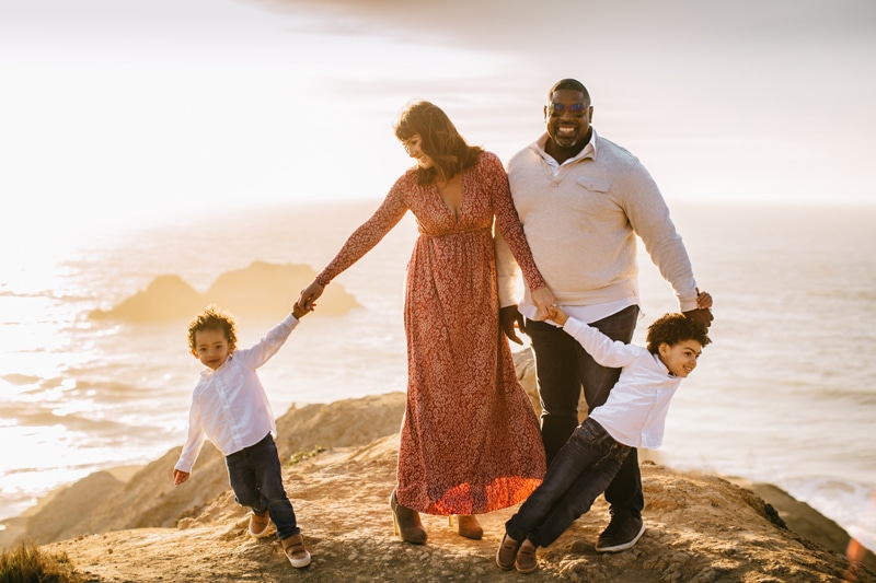 Family Photographer, family of 4 standing on cliff side next to ocean